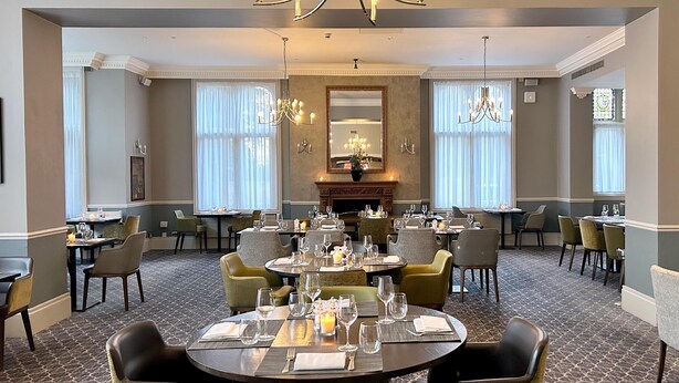 Une salle à manger élégante, avec plusieurs tables dressées pour les invités, de magnifiques lustres et une cheminée.