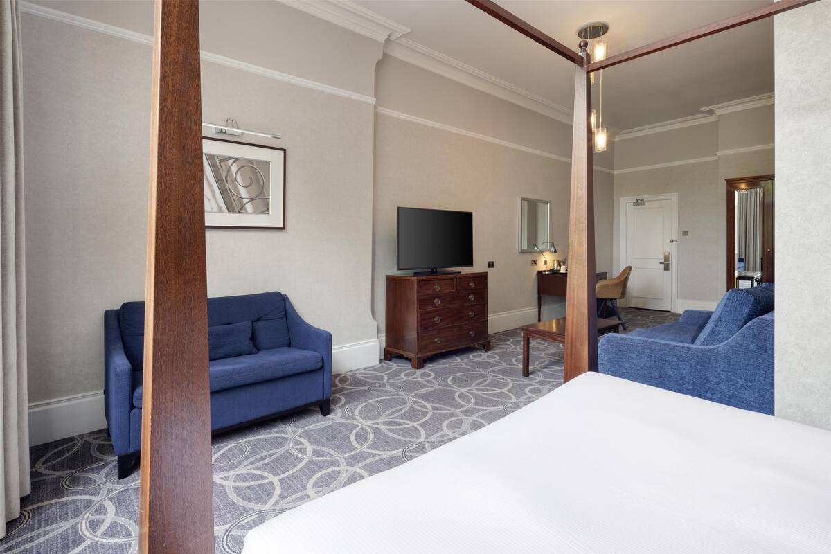 A hotel room with a large bed, two blue sofas, a wooden dresser, a television, and a mirror.