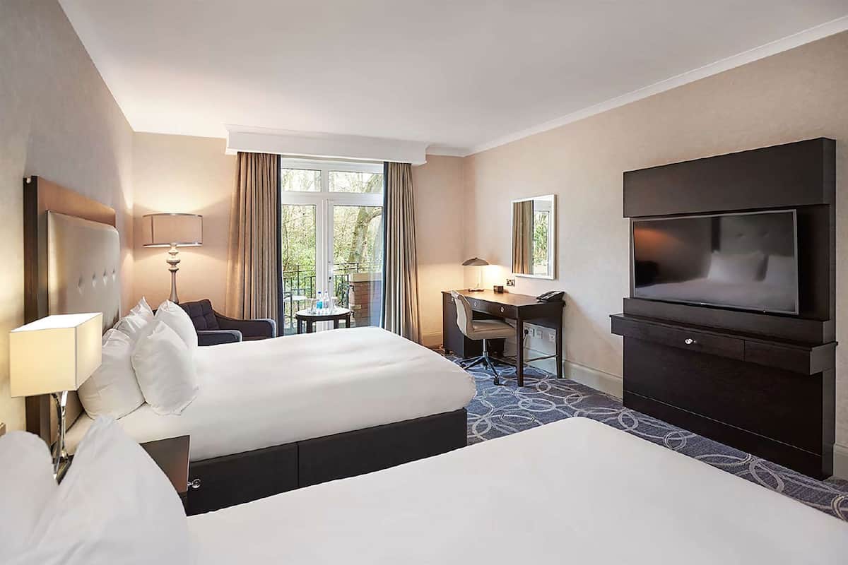 A hotel room with a large bed, a desk, a TV, and a window with curtains.