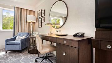 A hotel room with a desk, chair, TV, lamp, and a large window.