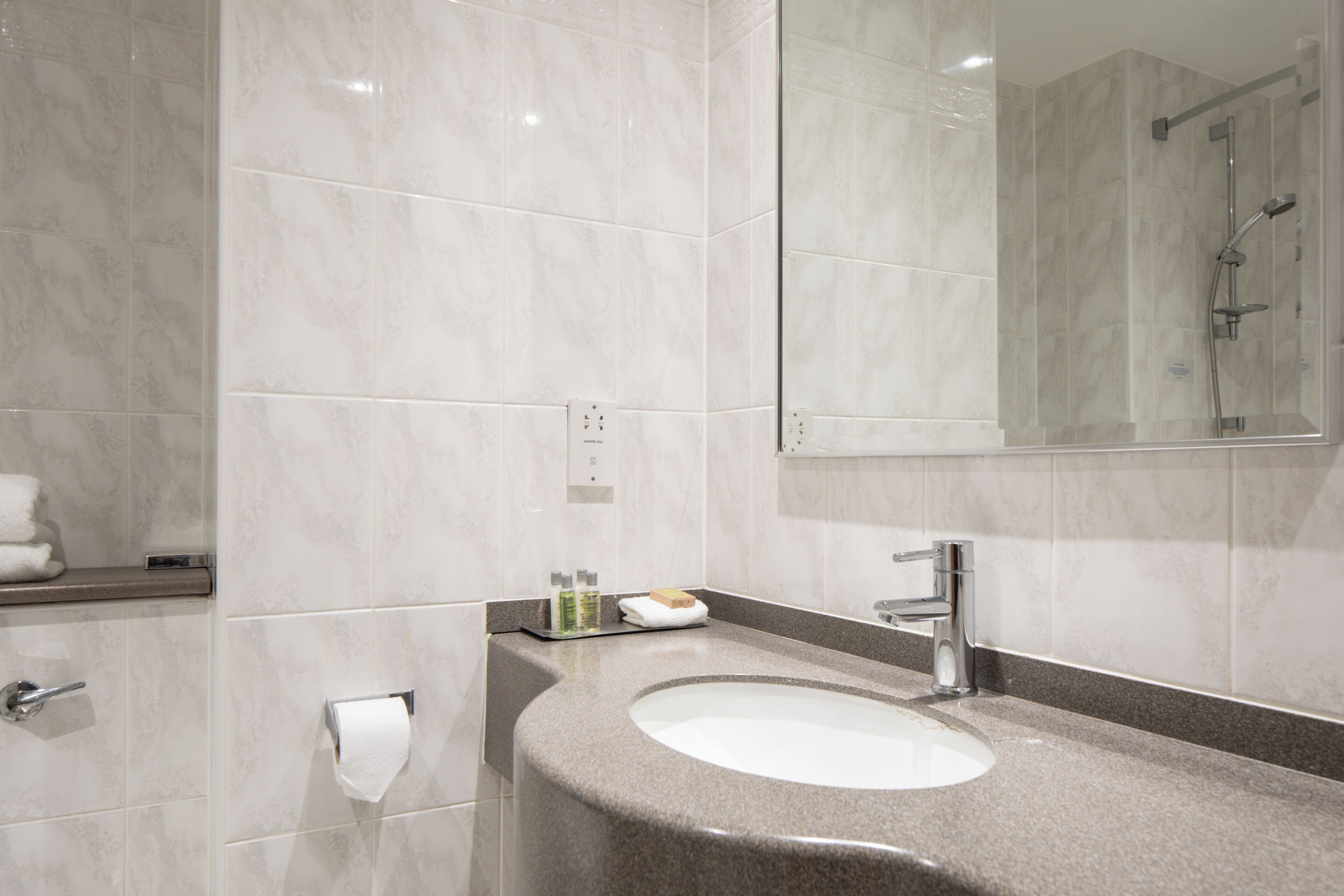 A modern bathroom with a granite countertop sink, a mirror, and a shower area.