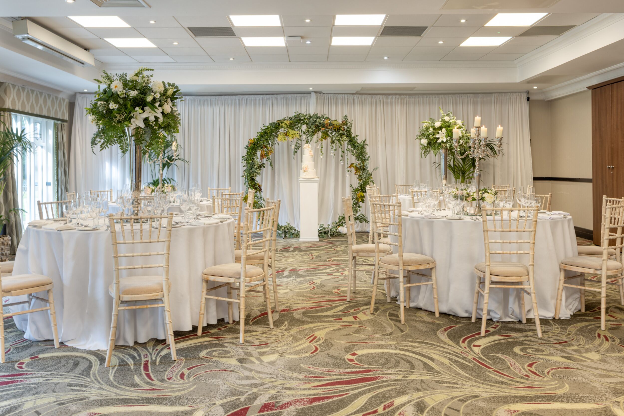 Une salle de banquet avec des tables rondes, des nappes blanches et des chaises de couleur claire.