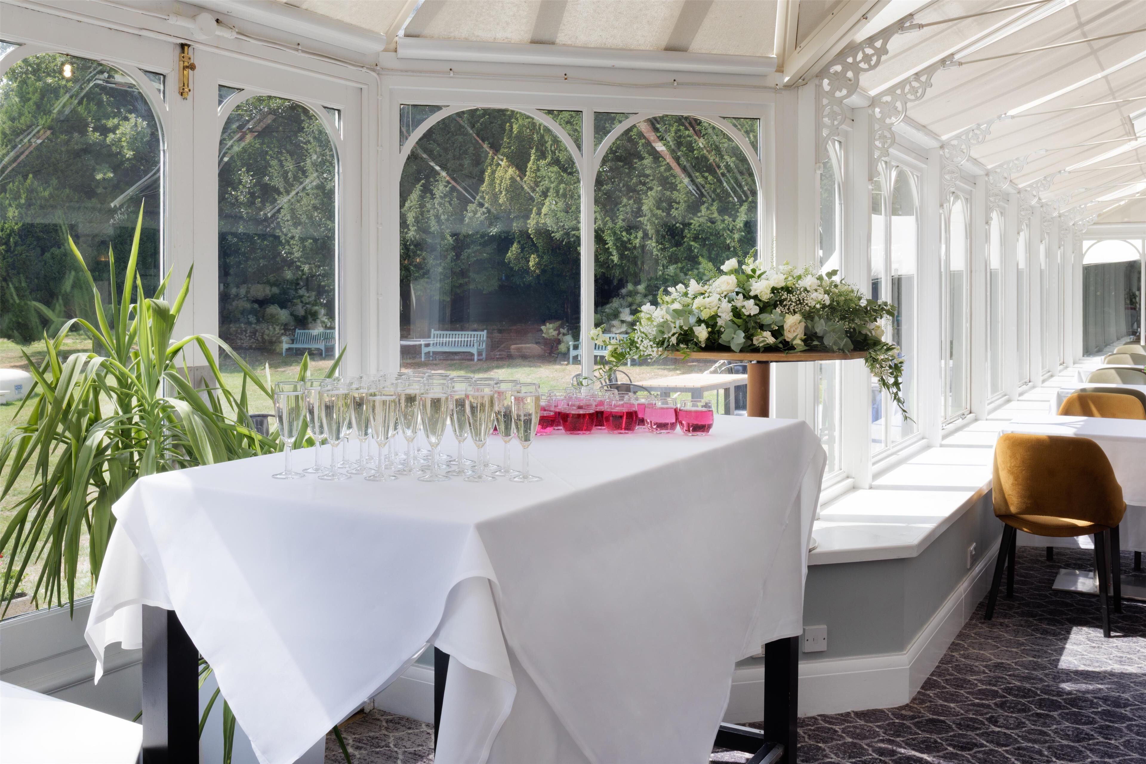 Ein Wintergarten mit gedecktem Tisch, umgeben von Stühlen und Blick auf Grünflächen.