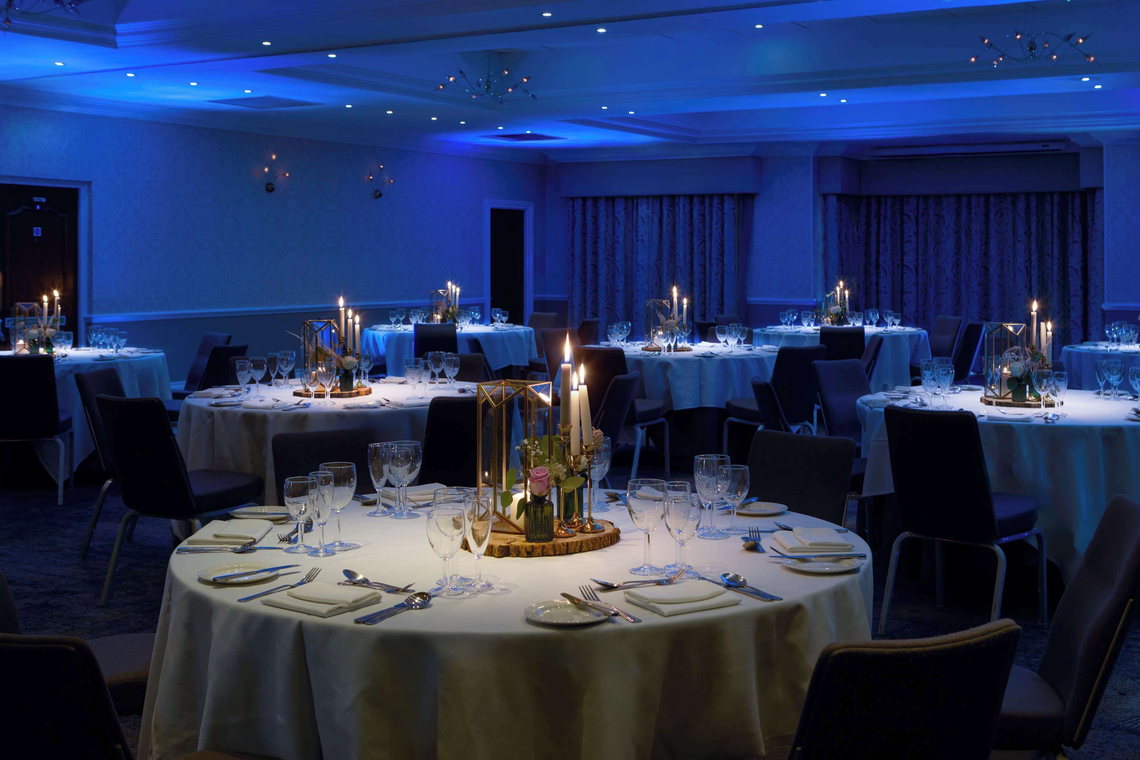 A banquet hall with round tables set for dining, each with candles and floral centerpieces.