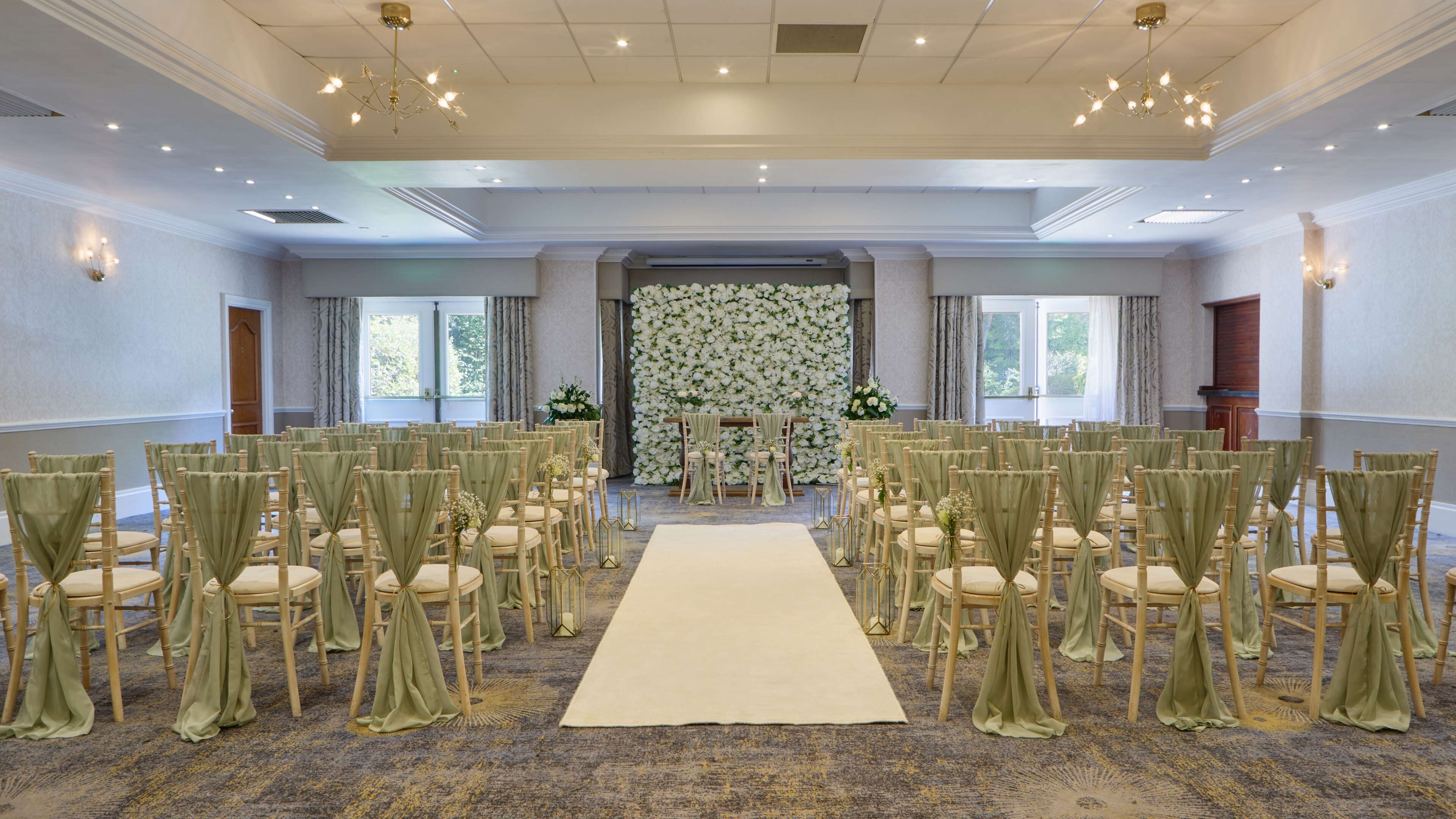 A formal room with rows of chairs, a central aisle, and a floral backdrop.