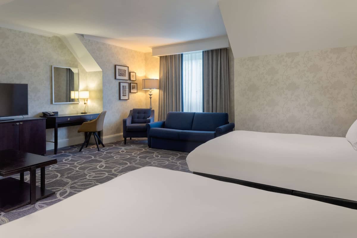 A hotel room with a bed, a desk with a chair, a sofa, a TV, and a lamp.