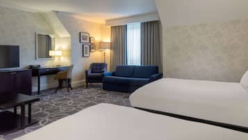 A hotel room with a bed, a desk with a chair, a sofa, a TV, and a lamp.