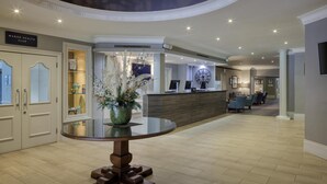 Un hall d’hôtel comprenant un comptoir d’accueil, une grande horloge et un espace salon.