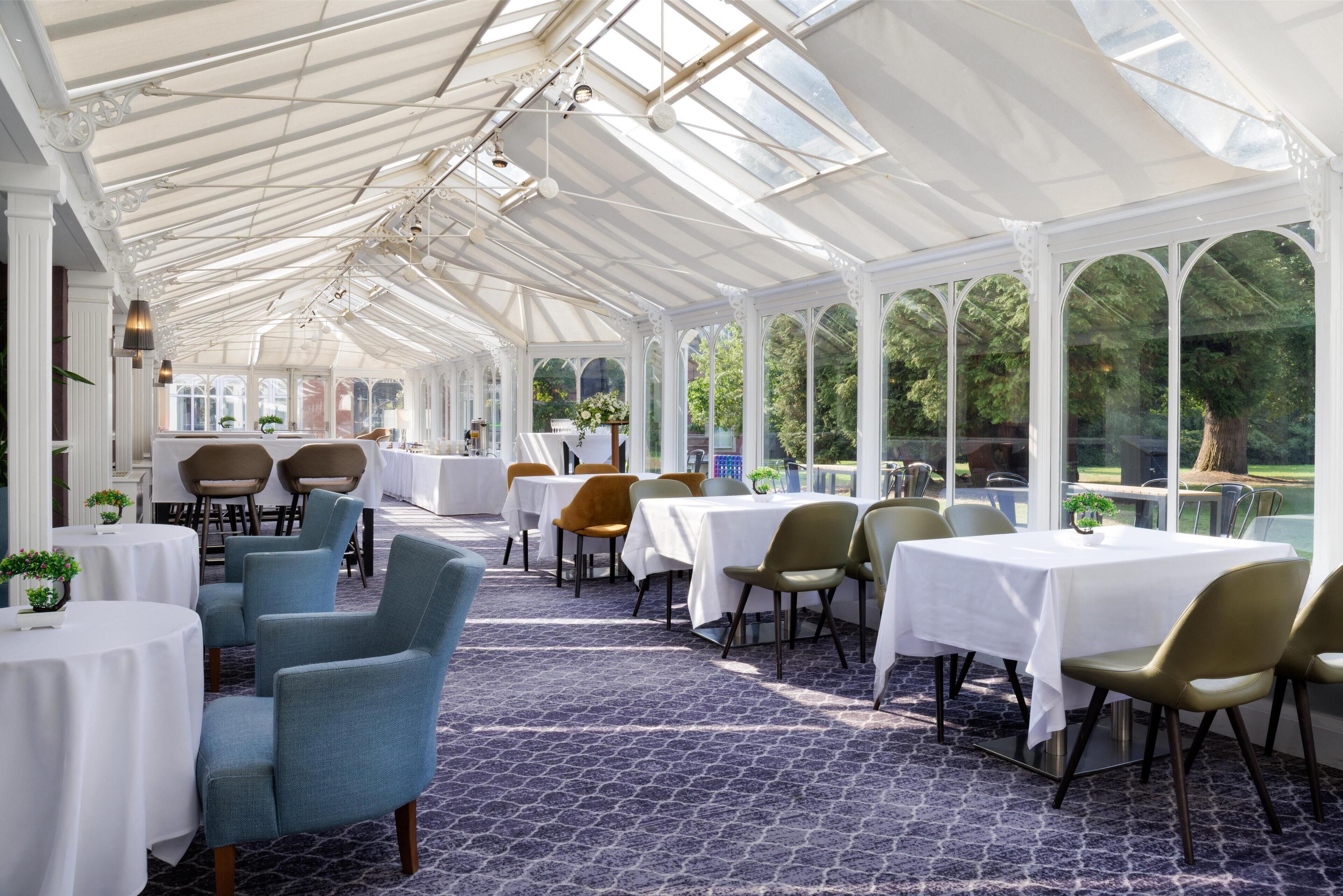 A conservatory with tables and chairs, large windows, and a patterned floor.