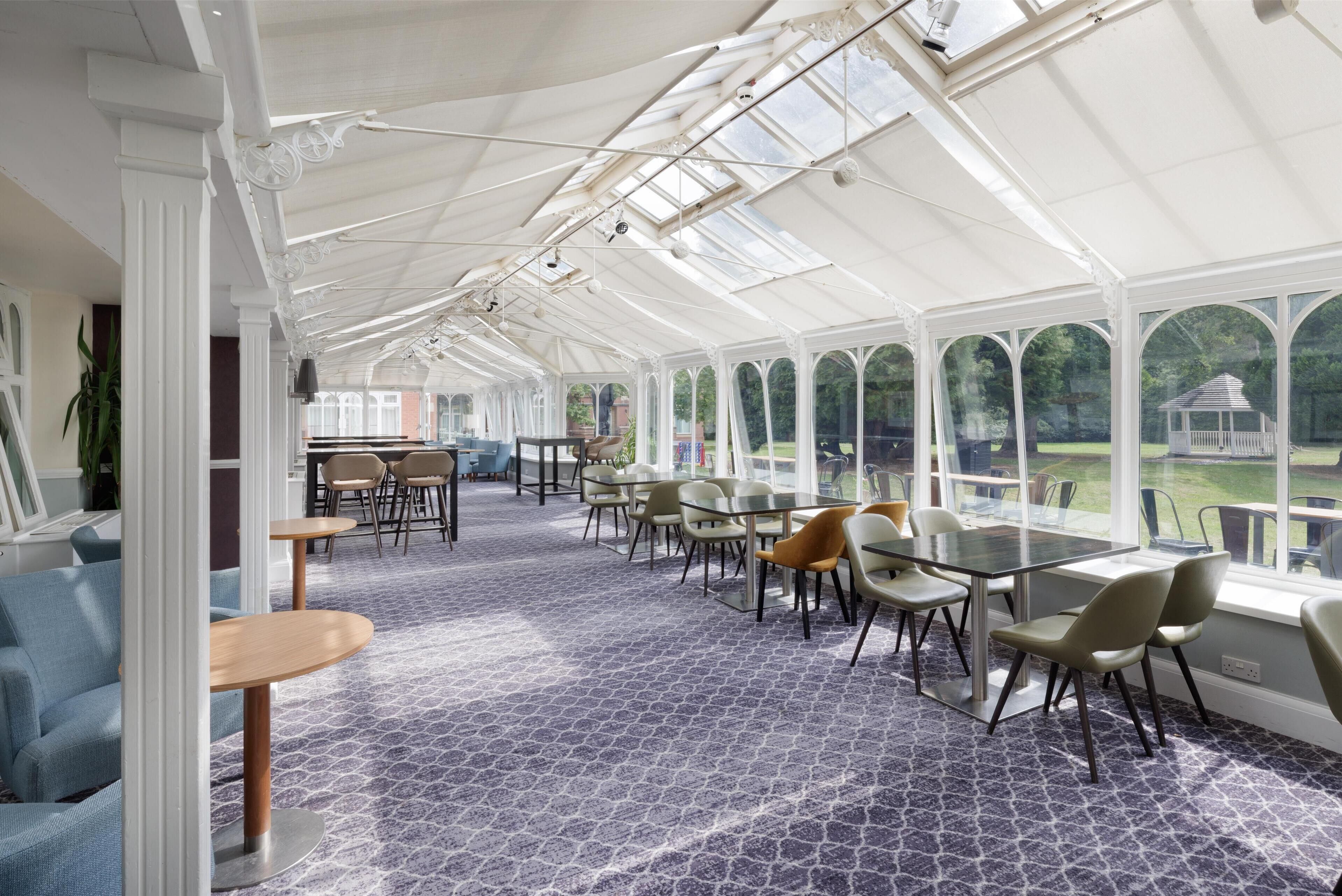 A conservatory with a patterned floor, tables, chairs, and a view of the garden.