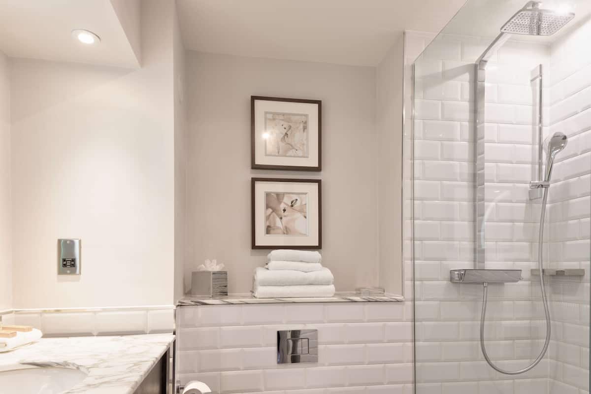 A modern bathroom with a glass-enclosed shower, white subway tiles, and two framed pictures on the wall.