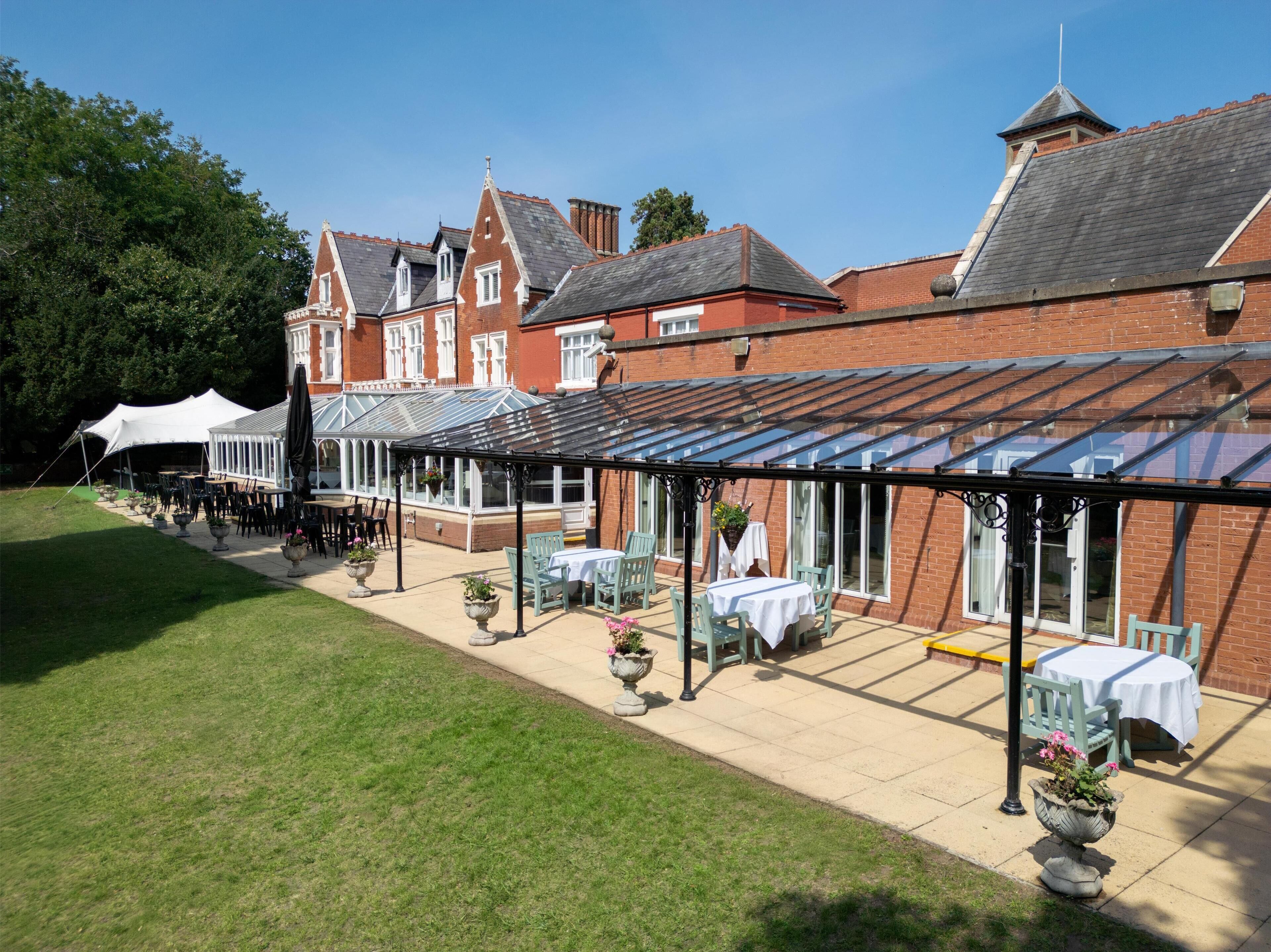 A courtyard with outdoor seating, a conservatory, and a large brick building with a pitched roof.