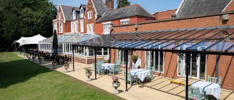 A courtyard with outdoor seating, a conservatory, and a large brick building with a pitched roof.