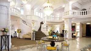 Eine prachtvolle Lobby mit einem runden Tisch in der Mitte, aufwendigen Treppenhäusern und klassischer Architektur.