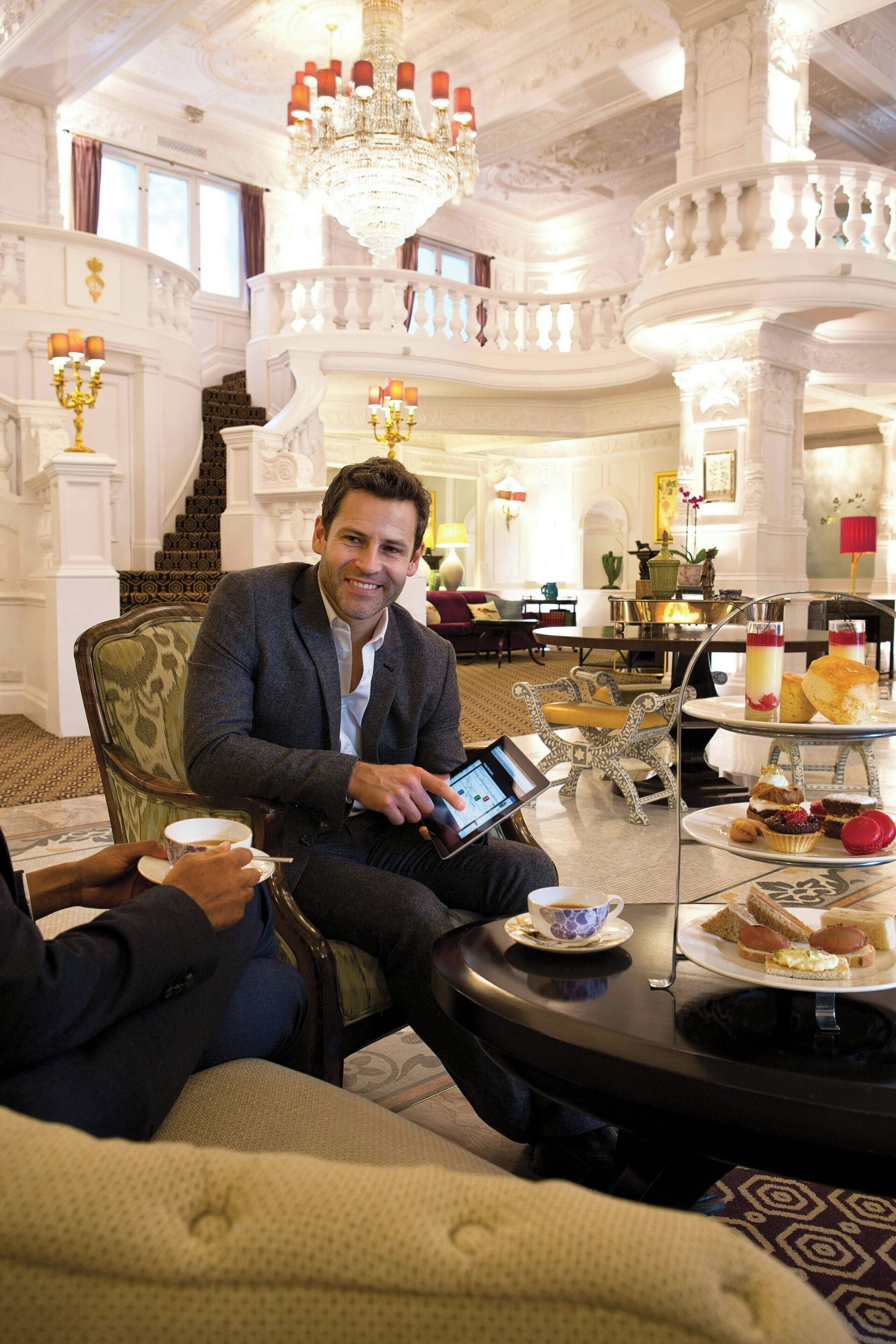 Un hall d’hôtel luxueux, doté d’une décoration somptueuse, d’un grand escalier et d’un présentoir à trois niveaux où sont exposés de délicieux desserts.
