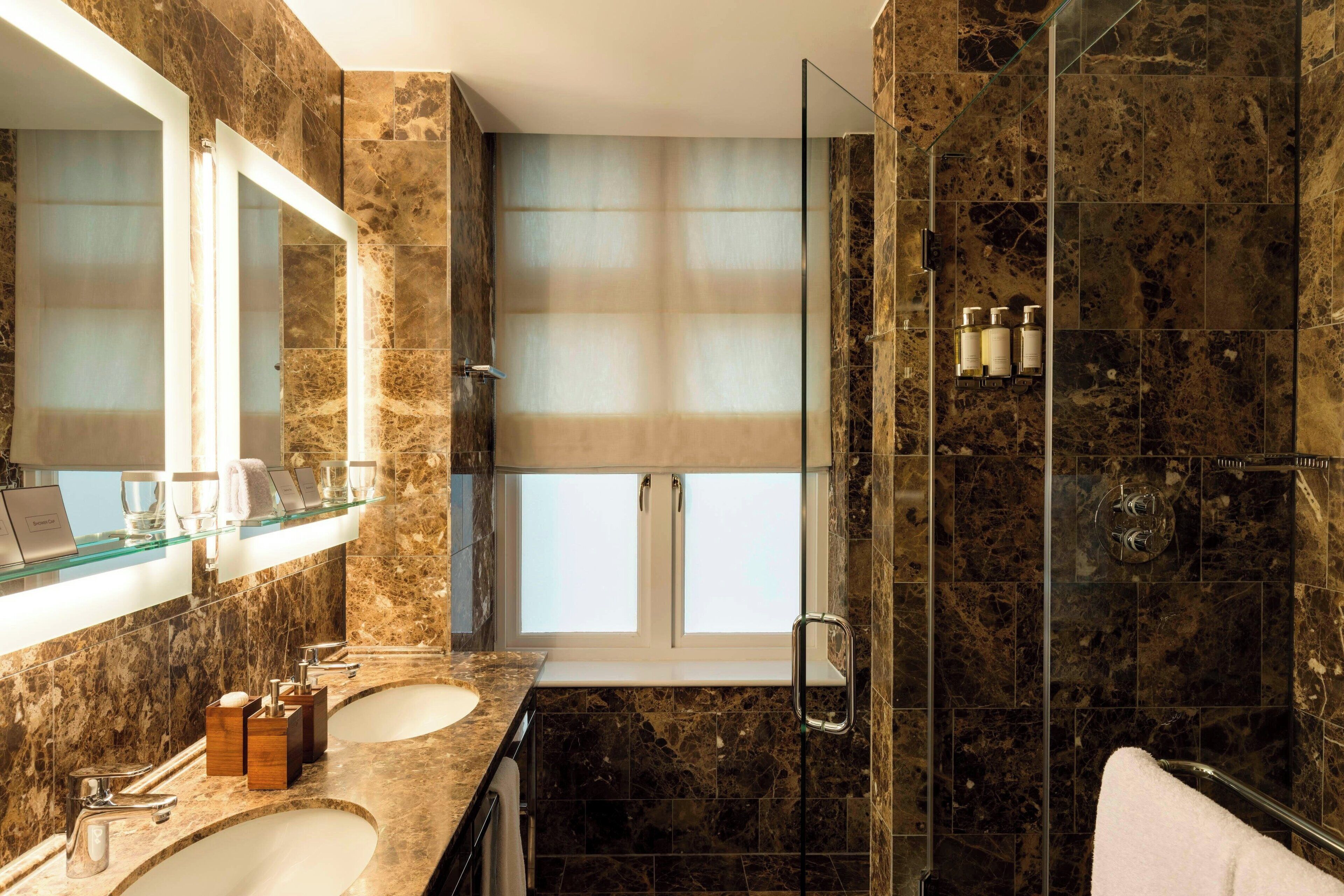 Une salle de bain moderne avec deux lavabos, une douche à l’italienne en verre et une grande fenêtre.