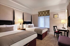 Hotelkamer met twee bedden, een bureau, een stoel, een televisie en een raam met gordijnen.