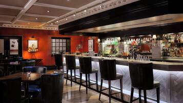 A bar area with a counter, stools, and a variety of bottles and glasses.