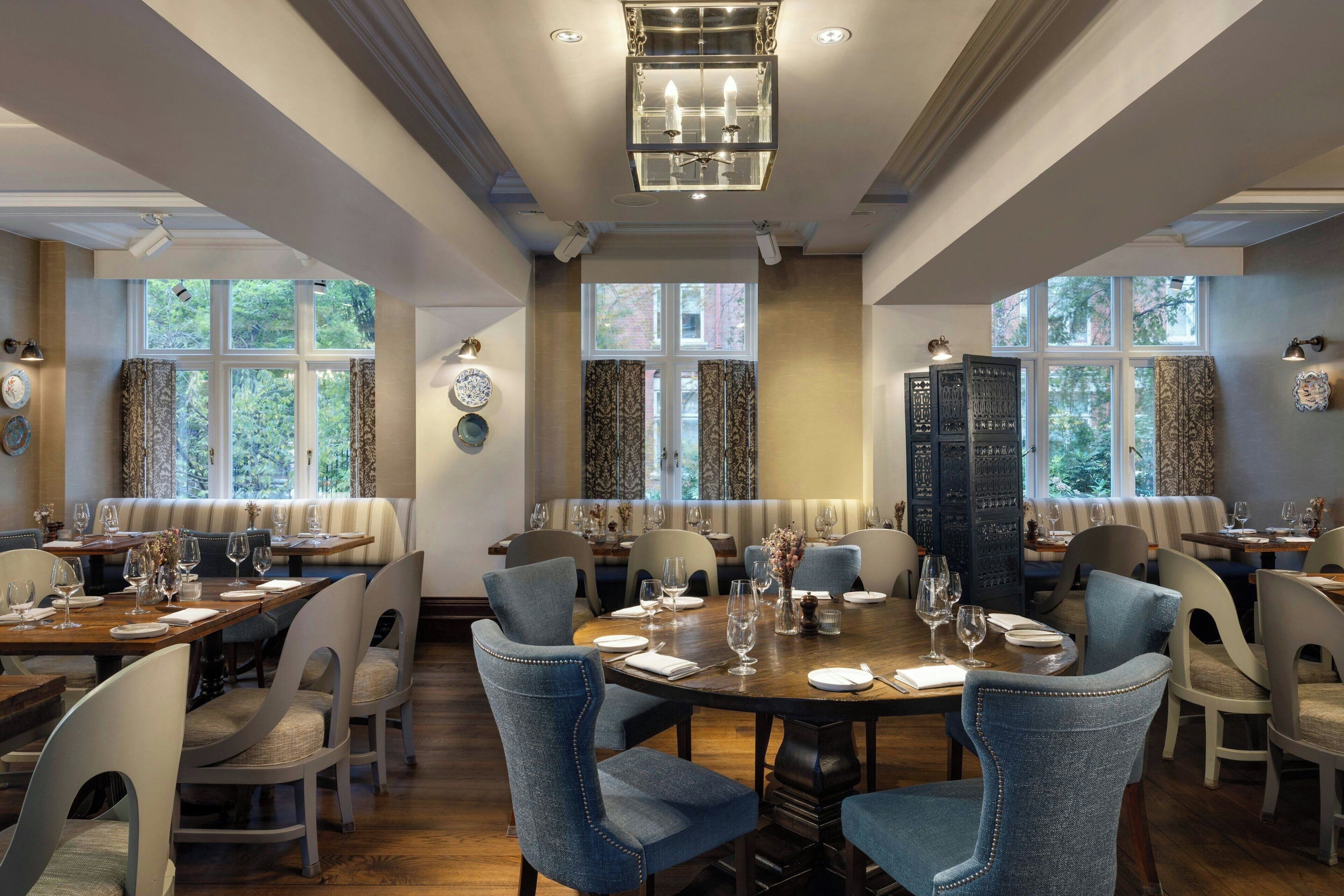 A dining area with round tables, blue upholstered chairs, and a chandelier.
