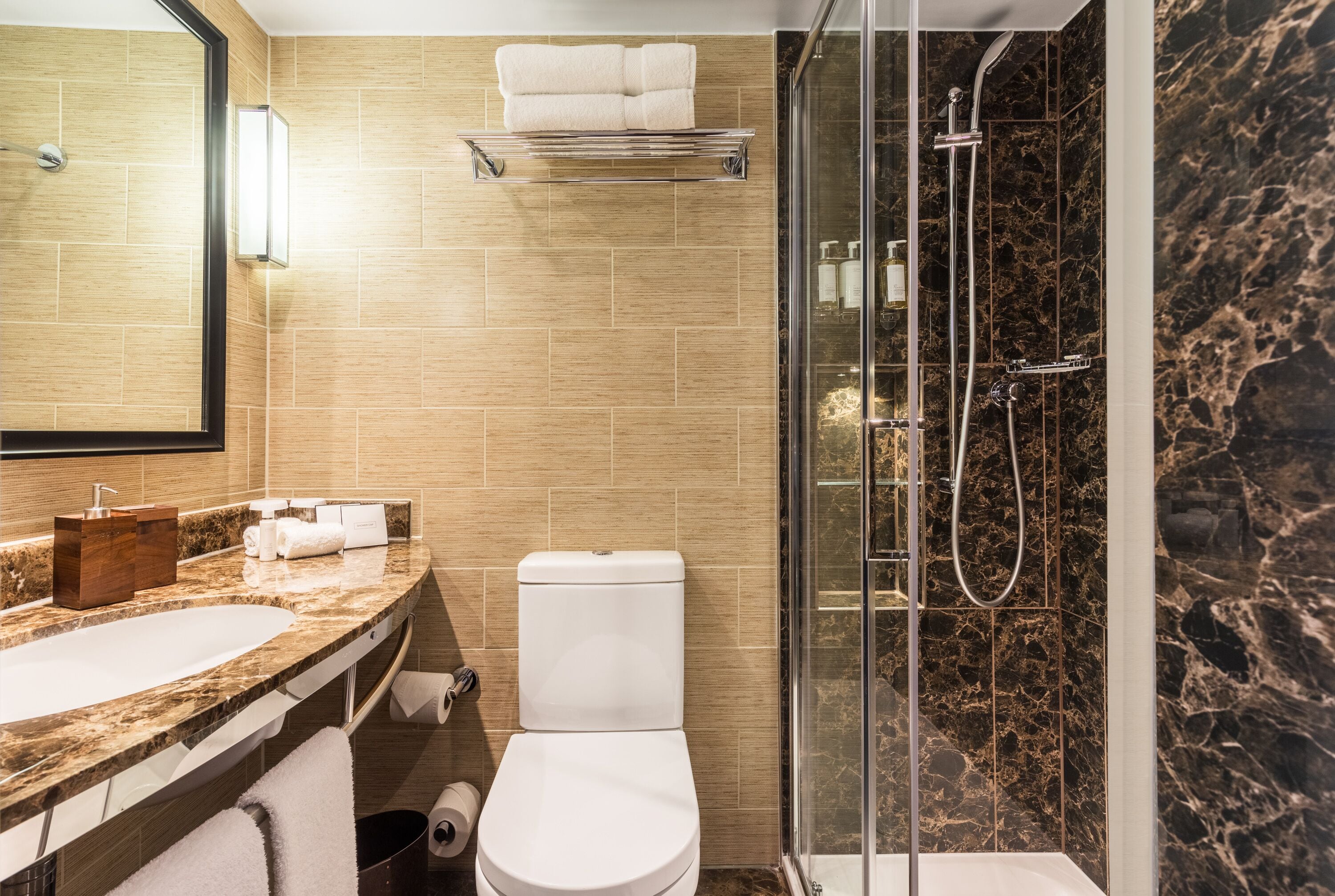 A modern bathroom with a marble sink, a toilet, and a glass-enclosed shower.
