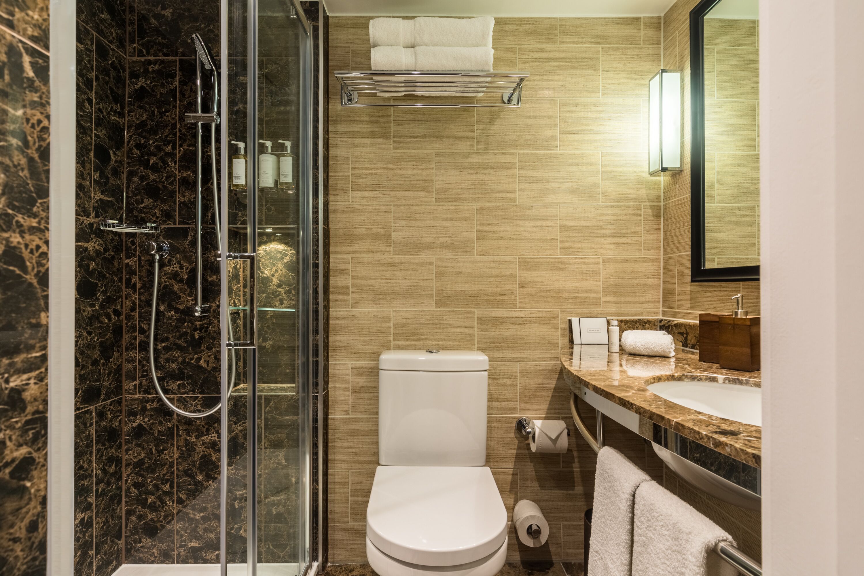 Une salle de bain moderne dotée d’une douche à parois de verre, de toilettes, d’un lavabo avec un plan de travail en marbre et d’un porte-serviettes.