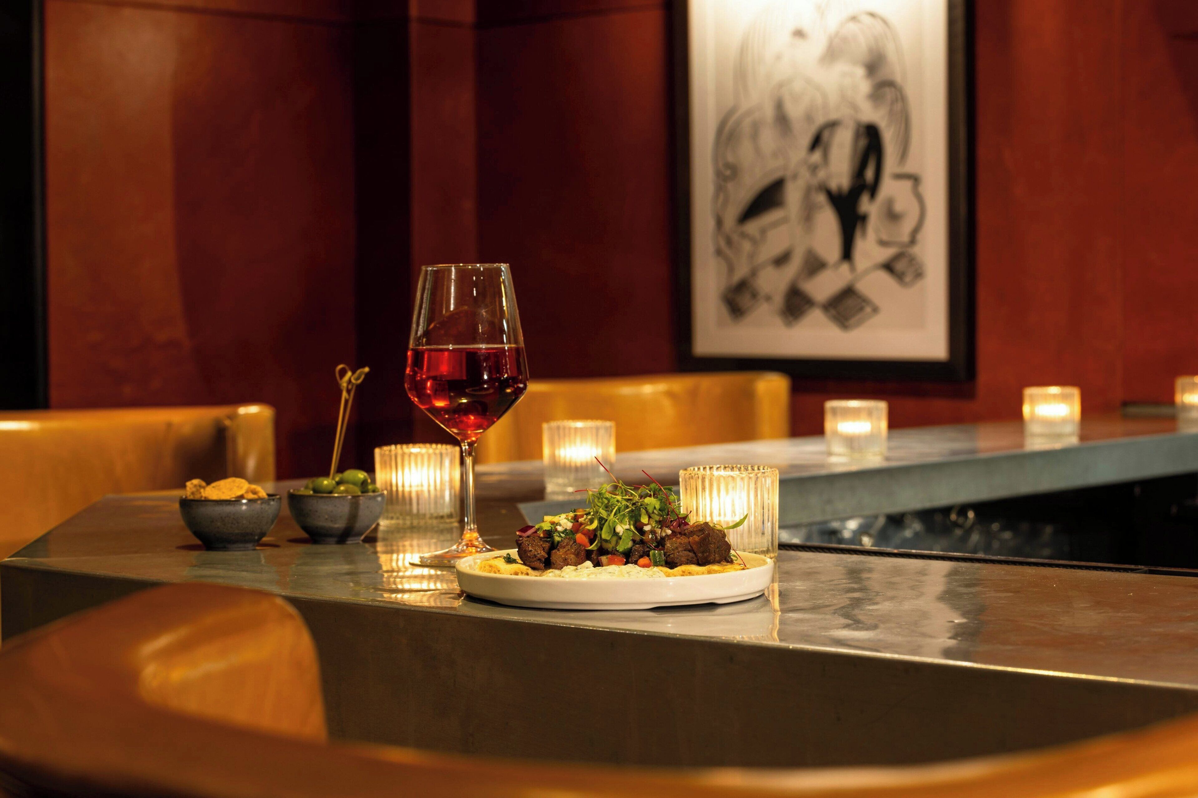 A dining table with a plate of food, a glass of red wine, and candles.