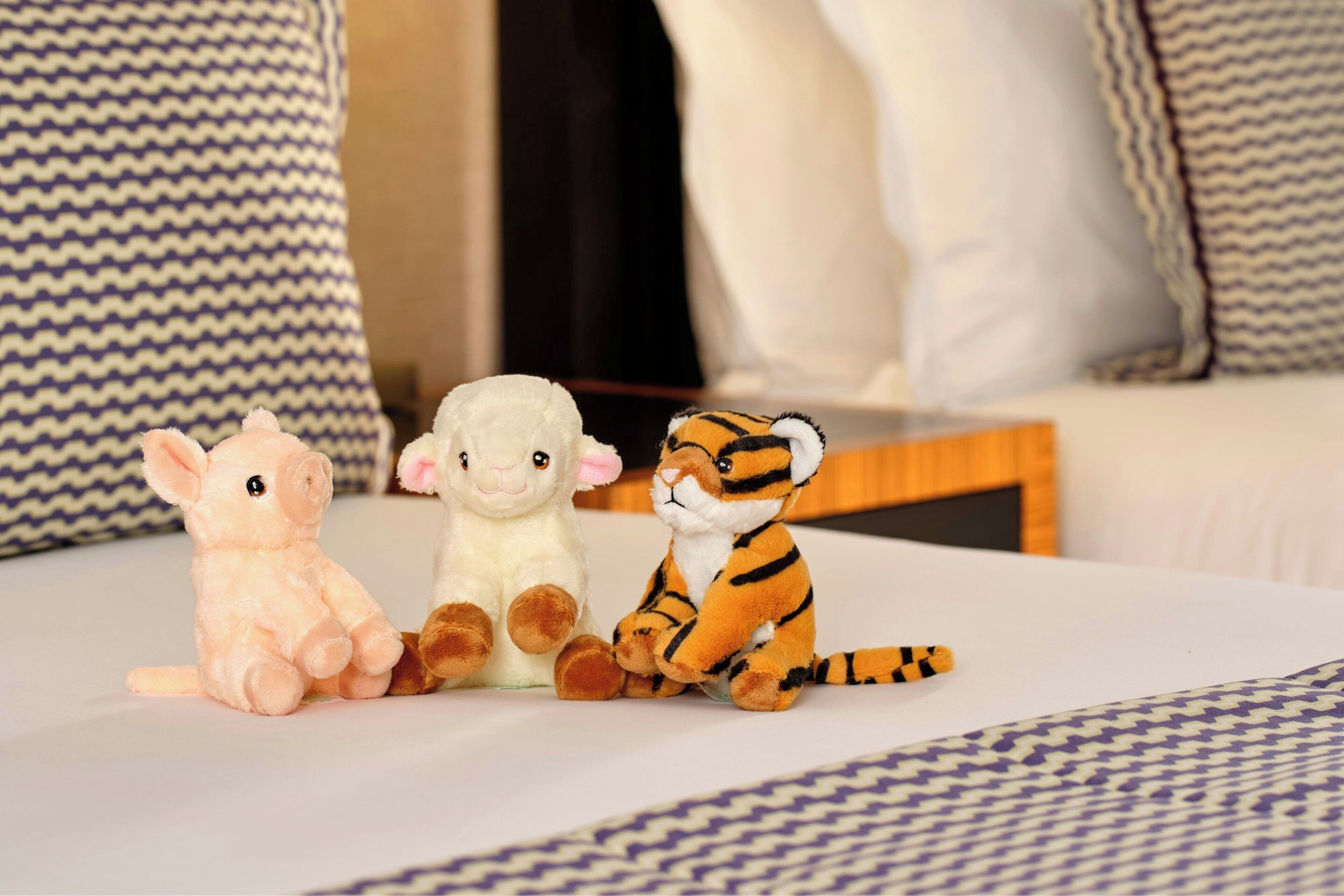 Three plush toys on a bed with patterned pillows.