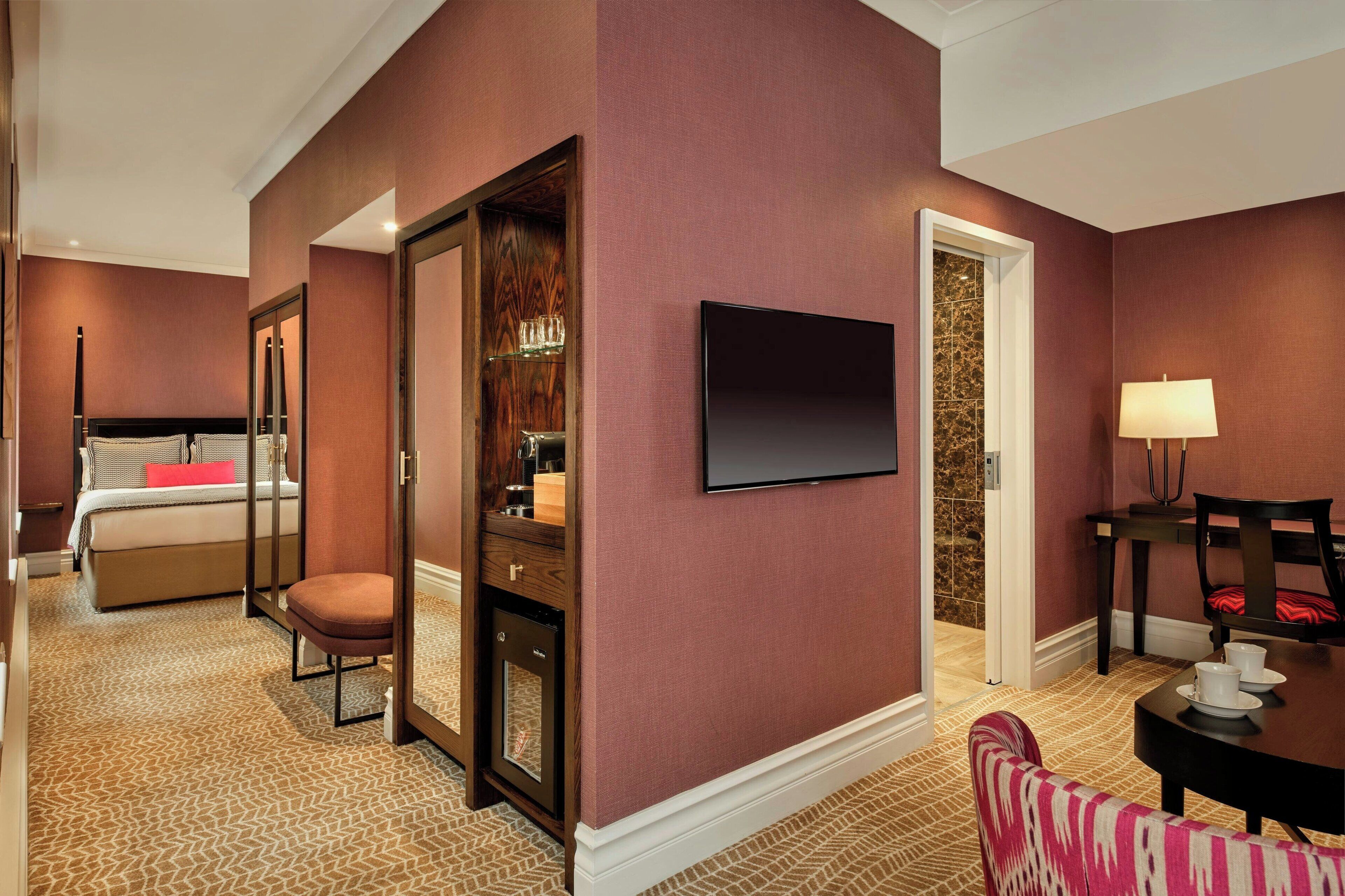 Una habitación de hotel con cama, zona de estar con mesa y sillas, televisor montado en la pared y armario con espejo.