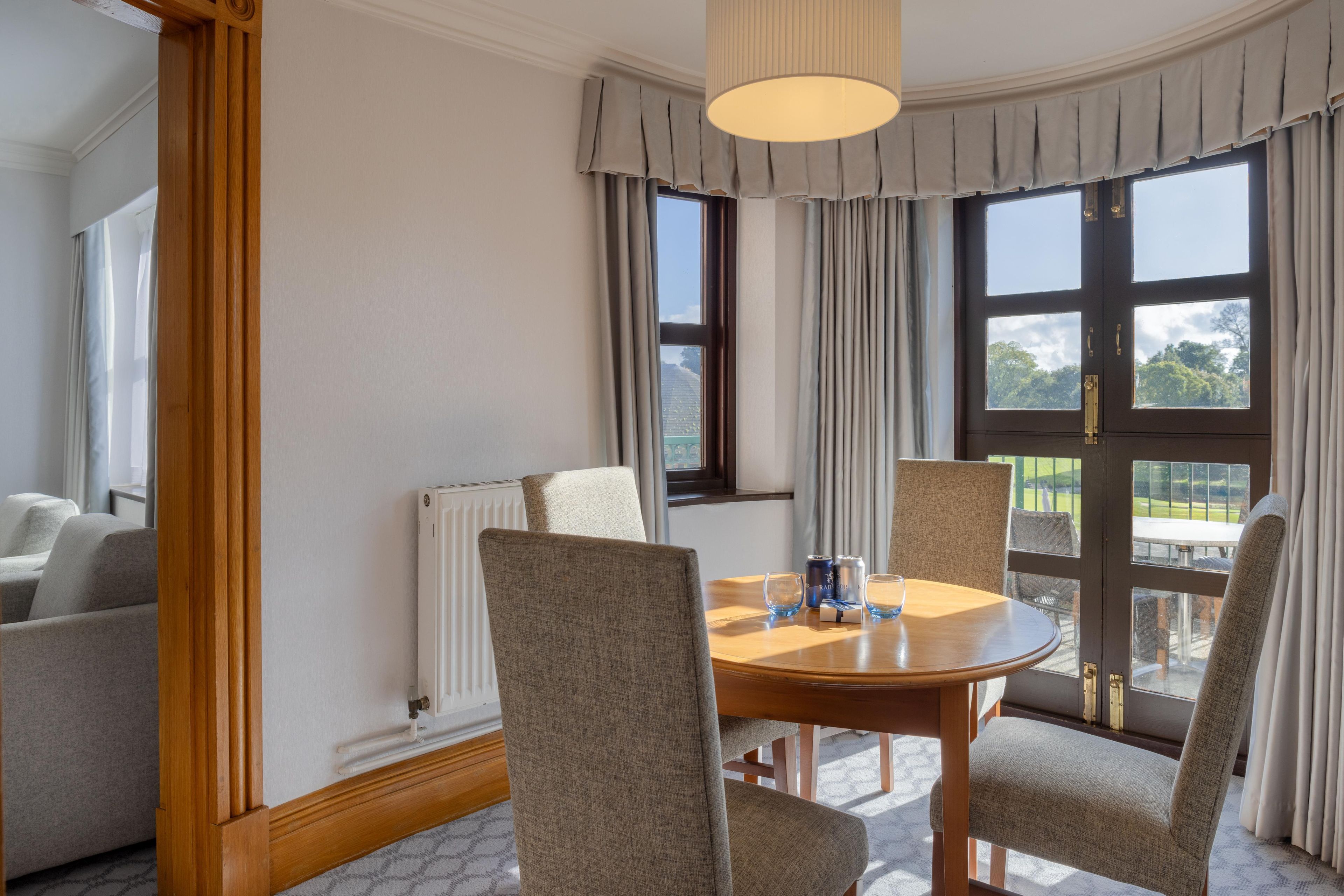 A dining area with a round table, four chairs, a radiator, and a view of the outdoors.