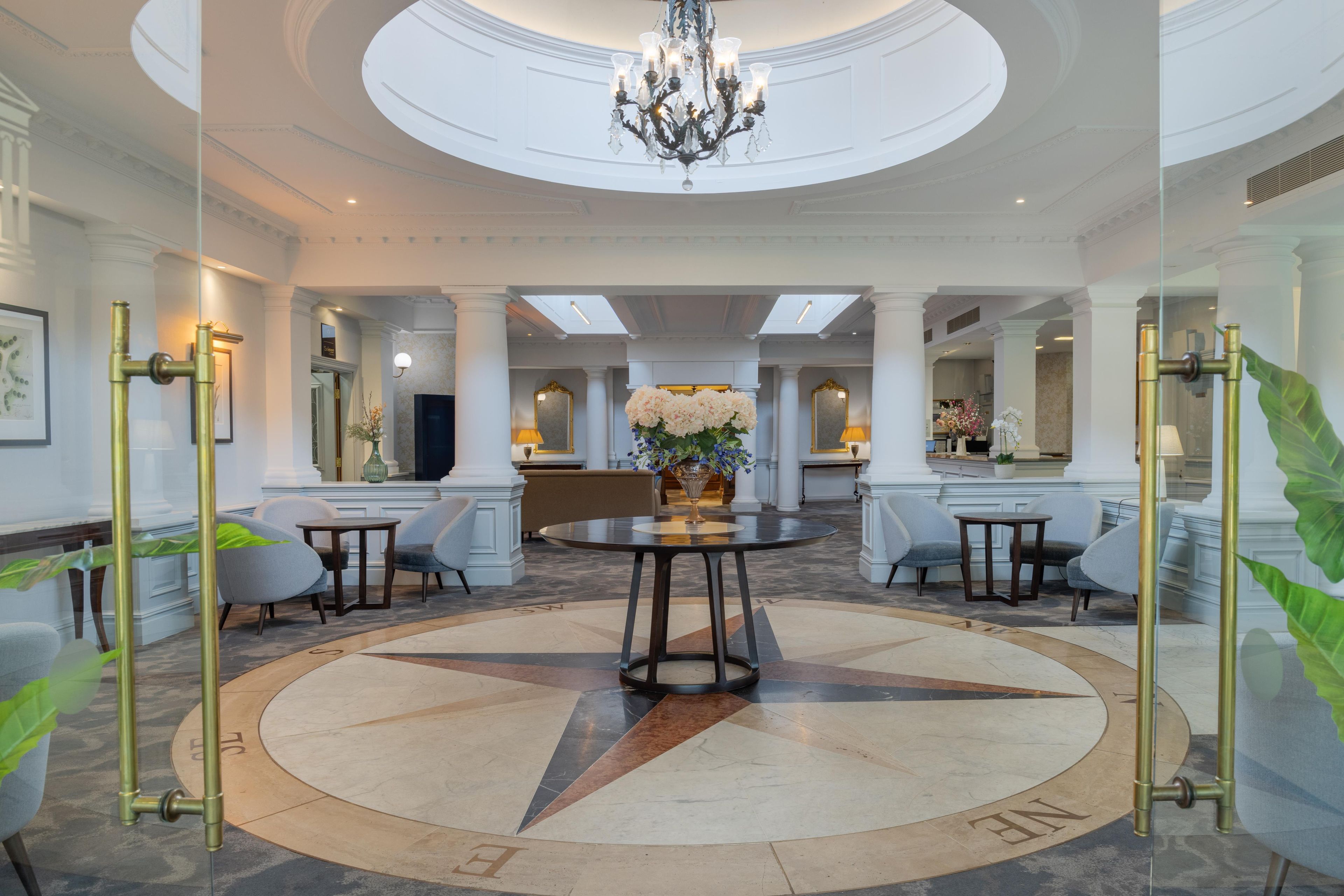 A spacious lobby with a central round table, seating arrangements, and a chandelier.