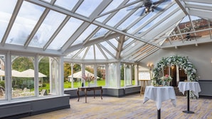 A conservatory with large windows, a patterned carpet, and a table with a vase. - Hilton Puckrup Hall Hotel & Golf Club, Tewkesbury (Tewkesbury)