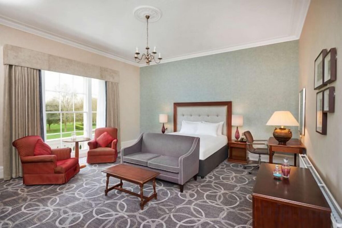 Una habitación de hotel con una cama, dos sillones, un sofá, una mesita y una lámpara.