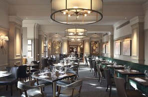 Een ruime restaurantruimte met meerdere eettafels en stoelen, elegante kroonluchters en een klassiek interieur.
