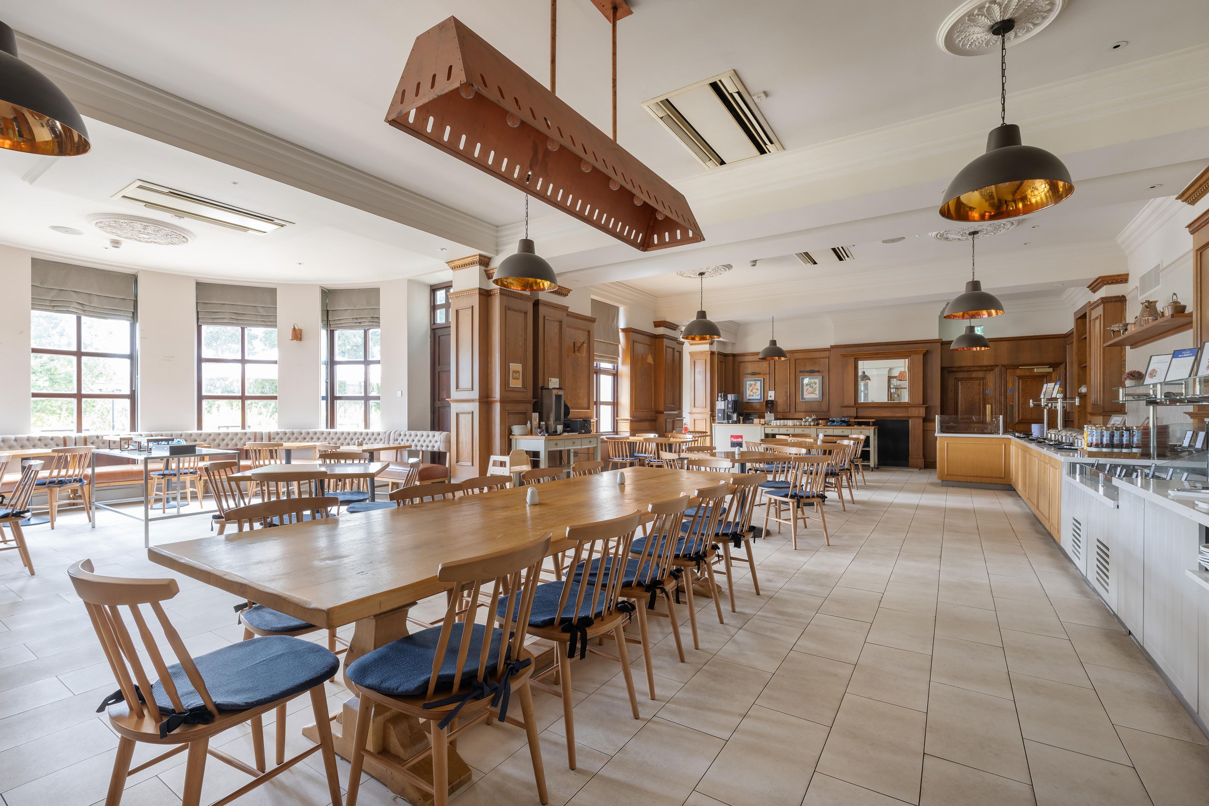 A spacious dining area with high ceilings, pendant lighting, and a long communal table surrounded by chairs.