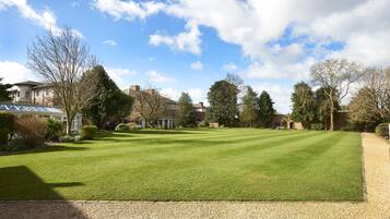 A well-maintained lawn with a gravel path, surrounded by mature trees and a few buildings in the background.