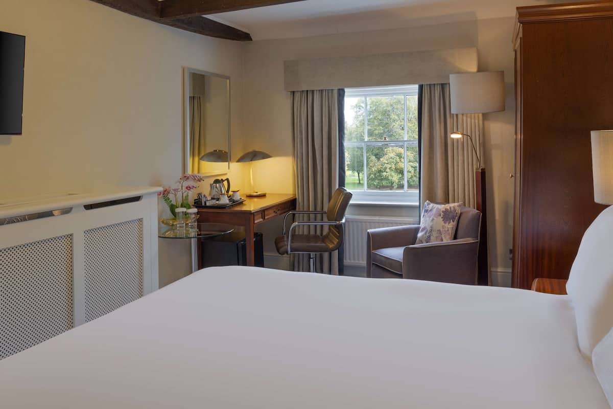 Een hotelkamer met een groot bed, een bureau met een lamp, een stoel en een raam met gordijnen.