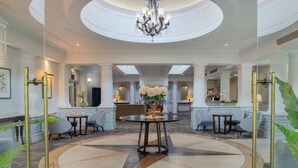 A spacious lobby with a central round table, a chandelier, and a large mirror. - Hilton Puckrup Hall Hotel & Golf Club, Tewkesbury (Tewkesbury)