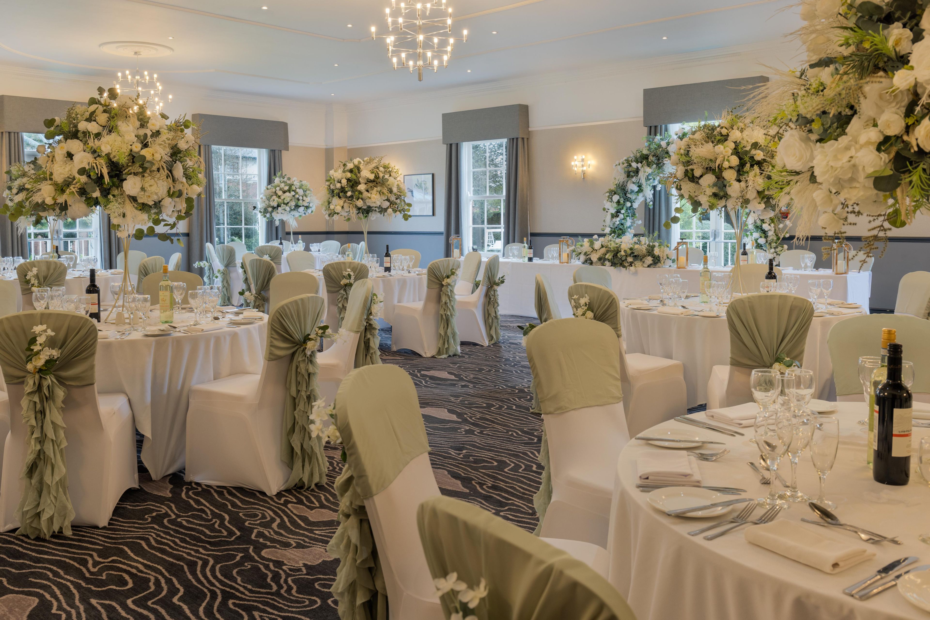 A banquet hall with round tables, chairs with green sashes, and large floral arrangements.