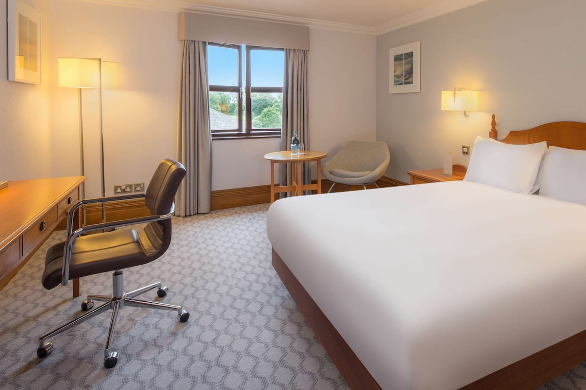 Een hotelkamer met een groot bed, een bureau met stoel, een klein rond tafeltje en een raam met gordijnen.