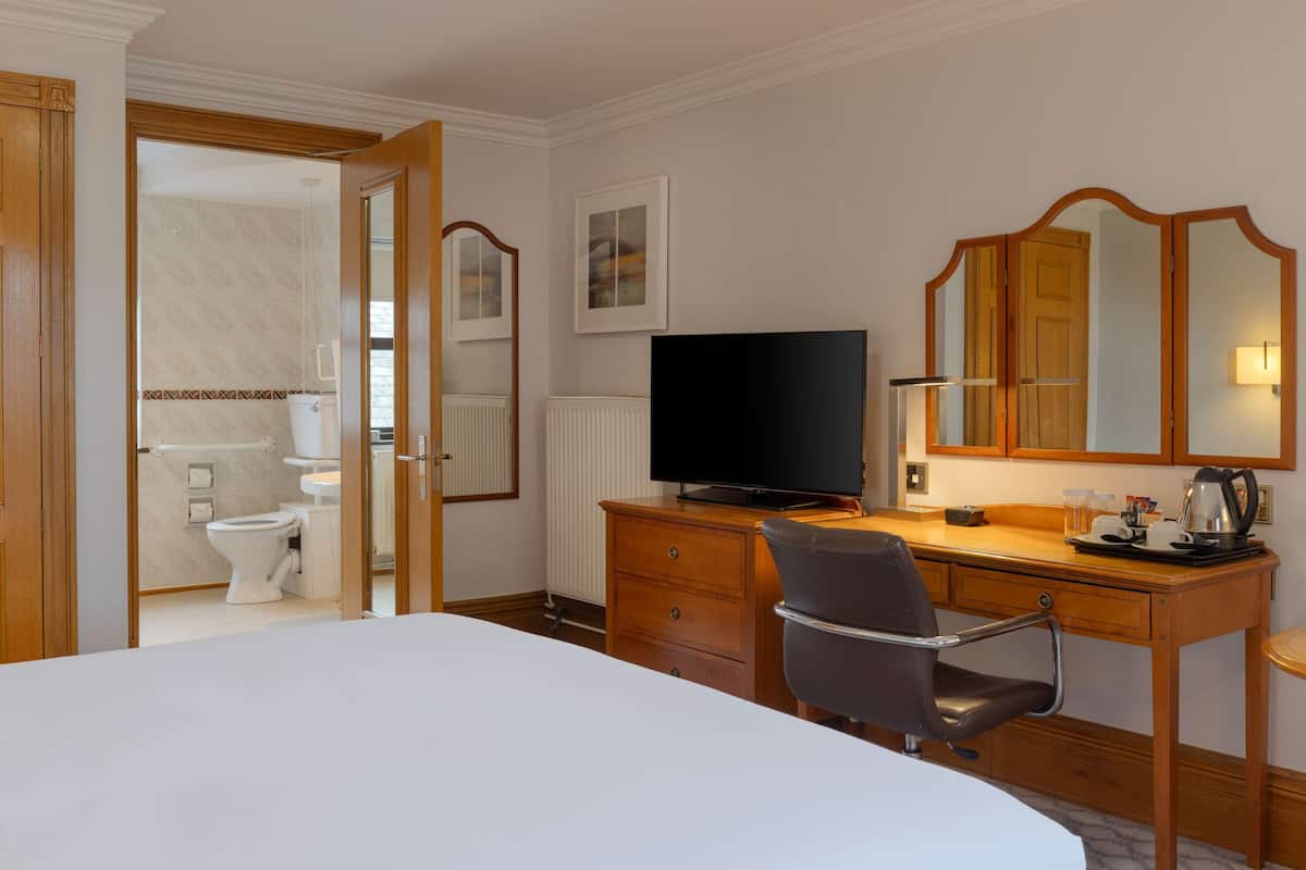 Hotelkamer met een bed, een bureau met stoel, een televisie, een spiegel, en een badkamer zichtbaar door een geopende deur.