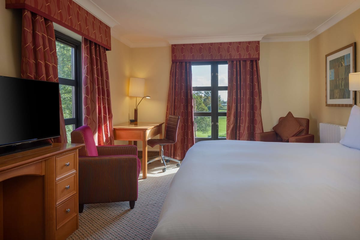Een hotelkamer met een groot bed, een bureau met stoel, een televisie en een raam met gordijnen.