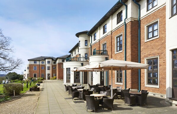 A courtyard with outdoor seating and a building with brick walls and multiple windows. - Hilton Puckrup Hall Hotel & Golf Club, Tewkesbury (Tewkesbury)