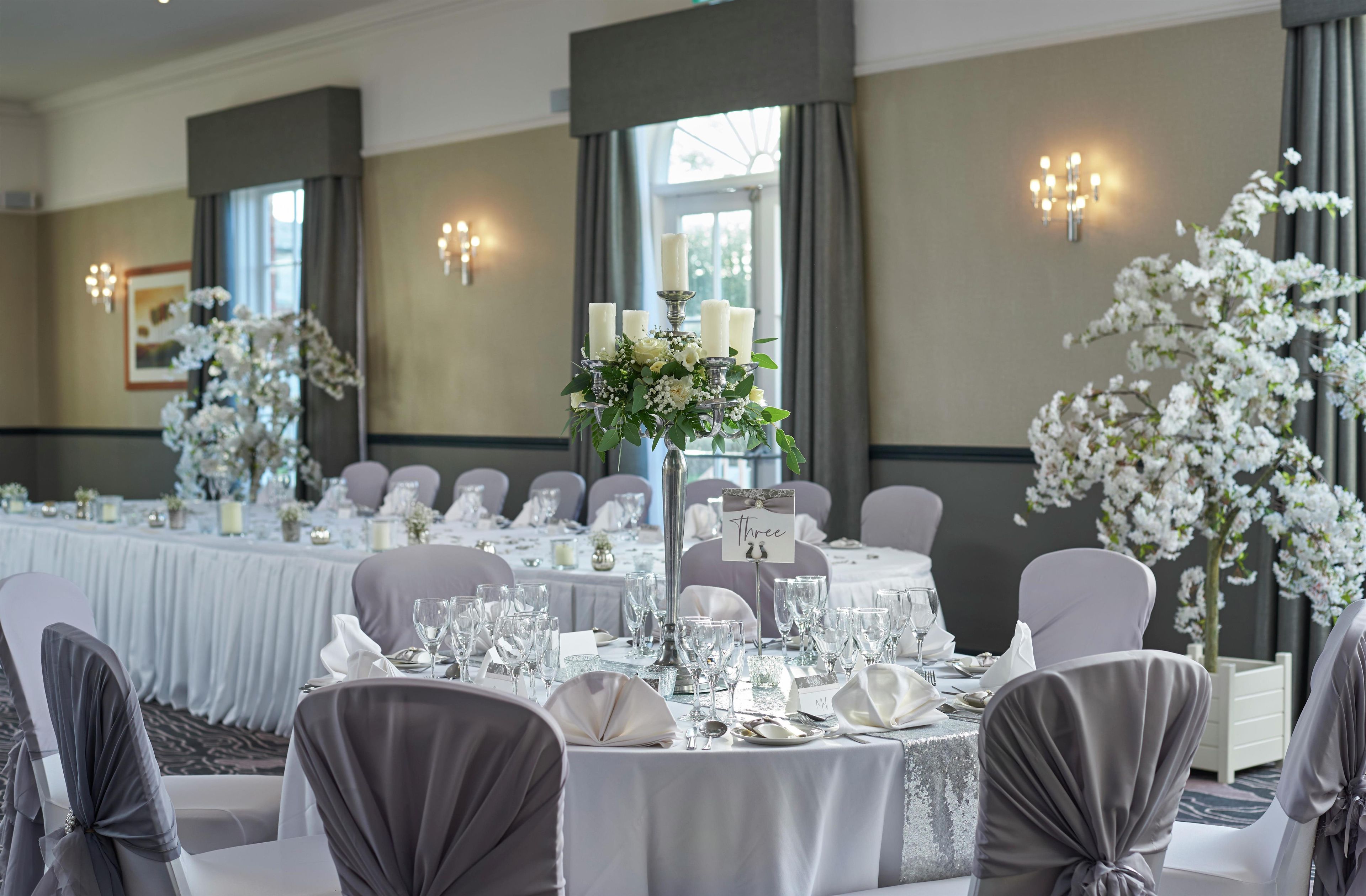 A banquet hall with round tables set for a formal event, featuring white tablecloths, glassware, and floral centerpieces.