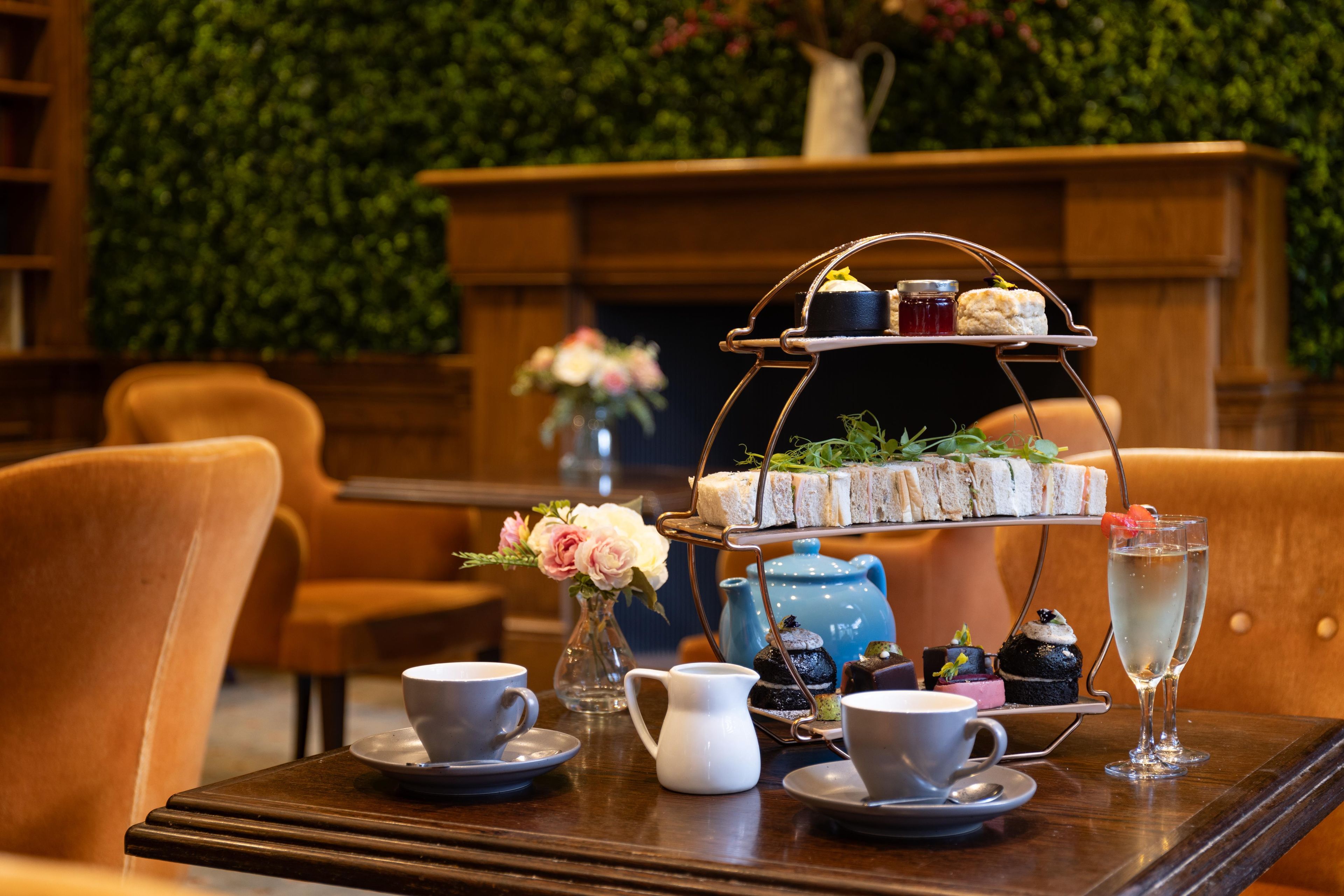 A table set with a tiered tea service, cups, a teapot, and a glass of water.