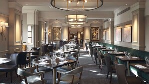 A spacious hotel dining area with multiple tables and chairs, elegant chandeliers, and framed artwork on the walls. - Hilton Puckrup Hall Hotel & Golf Club, Tewkesbury (Tewkesbury)