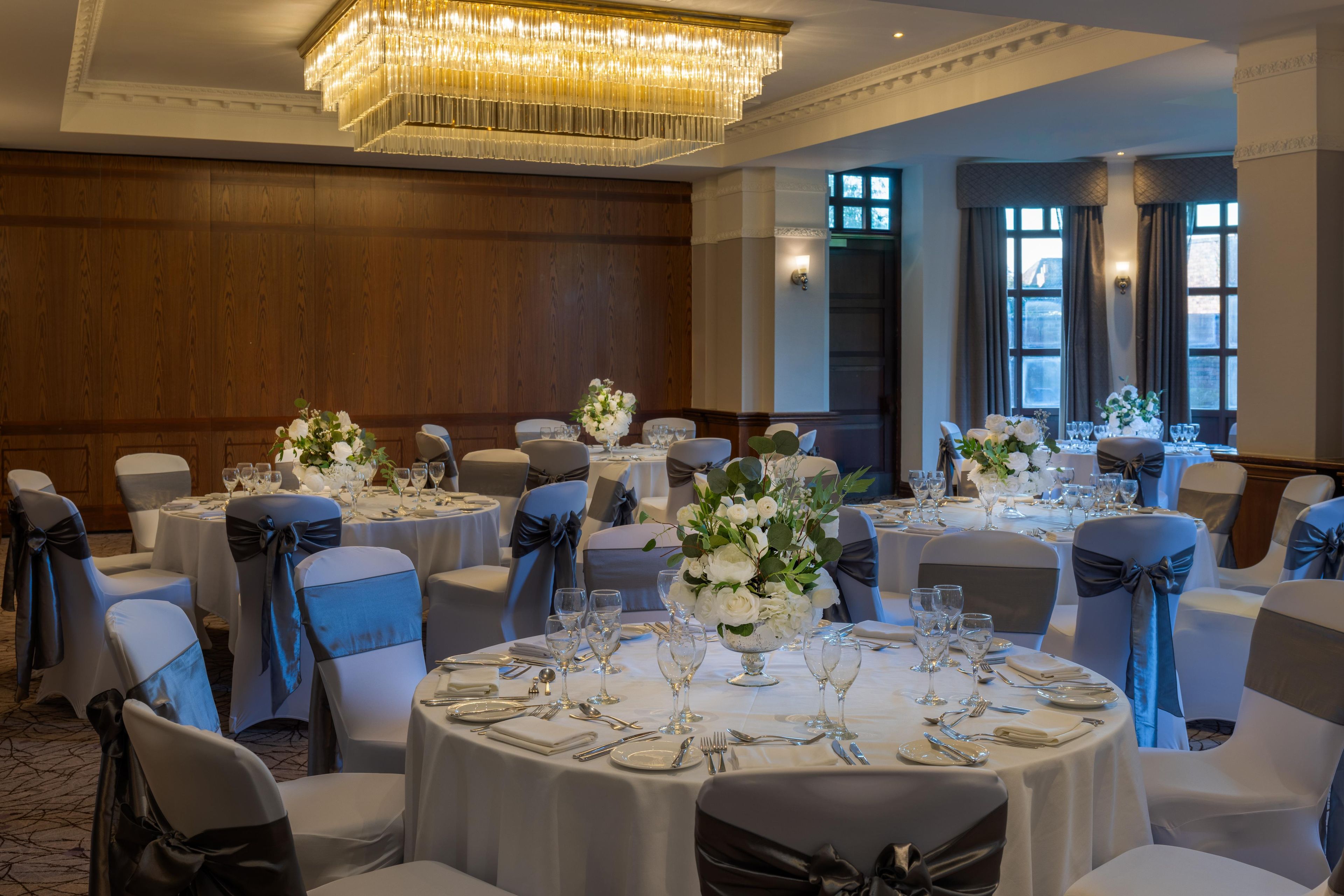 A banquet hall with round tables, chairs, and chandeliers.