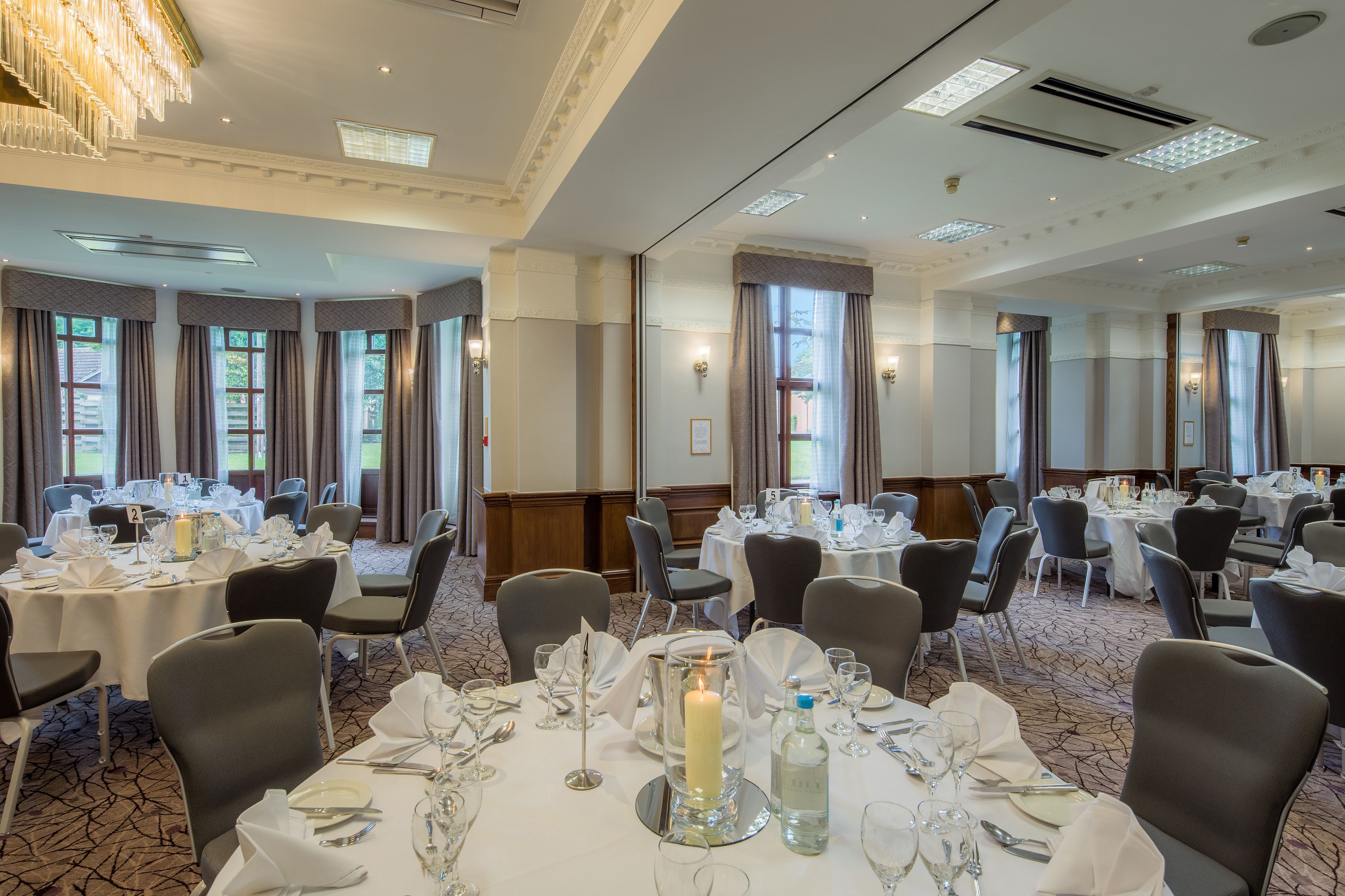 A banquet hall with round tables set for dining, featuring white tablecloths, candles, and glassware.