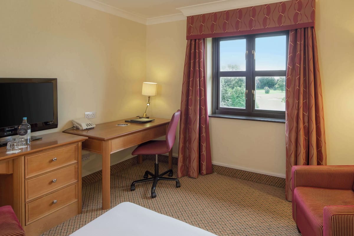 Een hotelkamer met een bureau, stoel, bed en uitzicht op de omgeving.