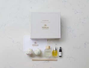 A Hilton Wellness Set box with a card, two wrapped items, a bottle of essential oil, a spray bottle, and chopsticks on a marble surface.