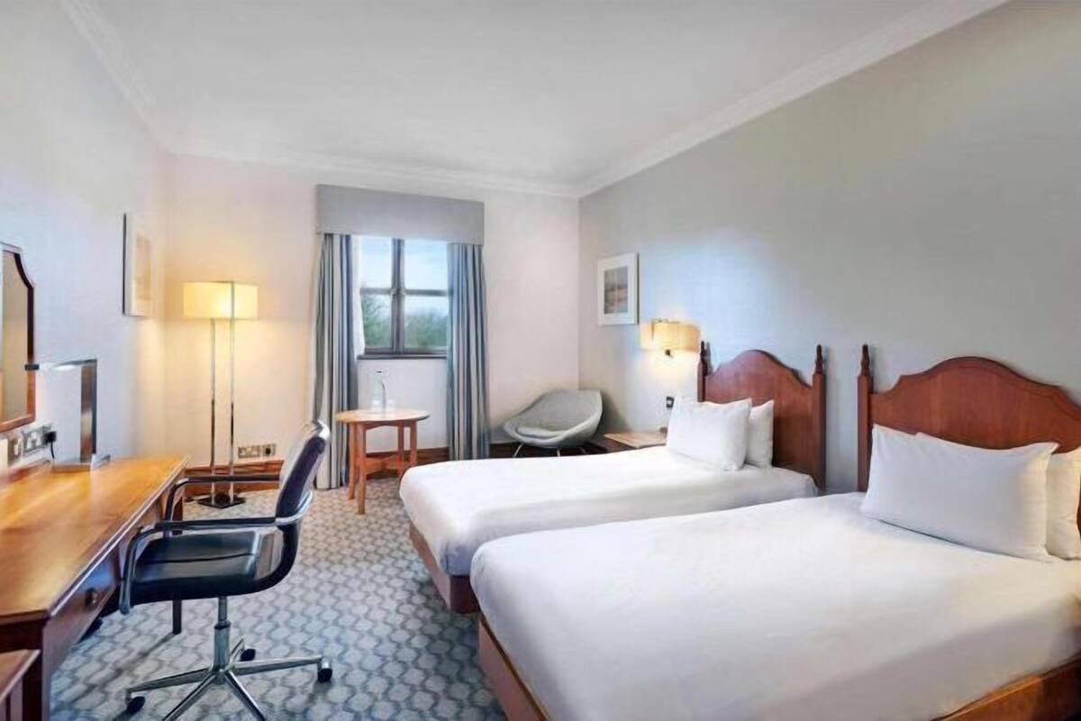 Een hotelkamer met twee bedden, een bureau, een stoel, een lamp en een raam.